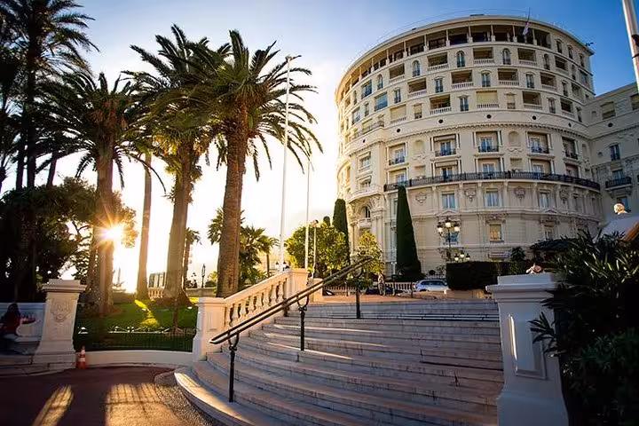 Grand curved white hotel building with palm trees and marble staircase in Monte Carlo Monaco at sunset