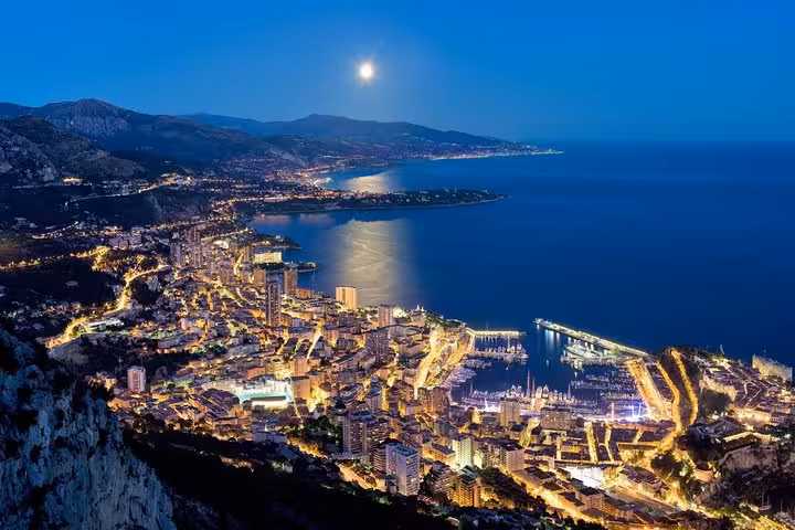Breathtaking night panorama of Monte-Carlo under a full moon, showcasing vibrant city lights and the coastline.