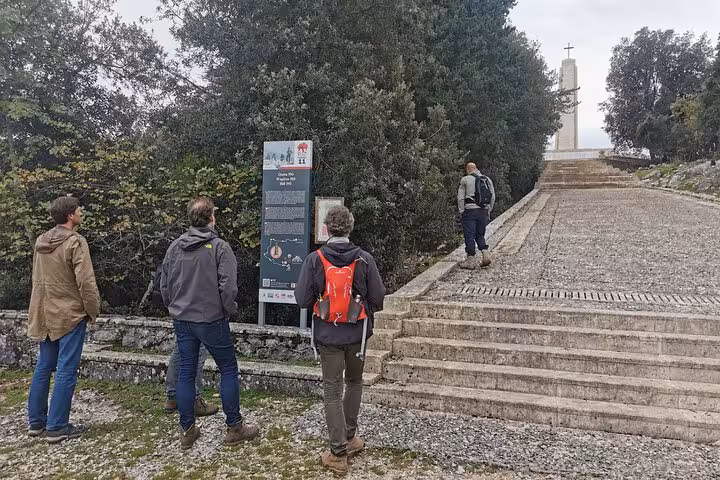 Hikers reading a trail sign at Monte Cassino battlefield with a historic monument and cross in the background