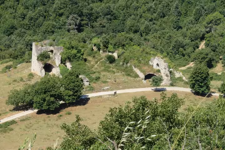 Ancient stone ruins and arched bunkers on Monte Cassino battlefield surrounded by lush green hills and mule tracks