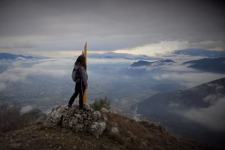 Solo hiker stands on Monte Cassino summit rock with panoramic cloudy valley views on a historic battlefield hiking tour