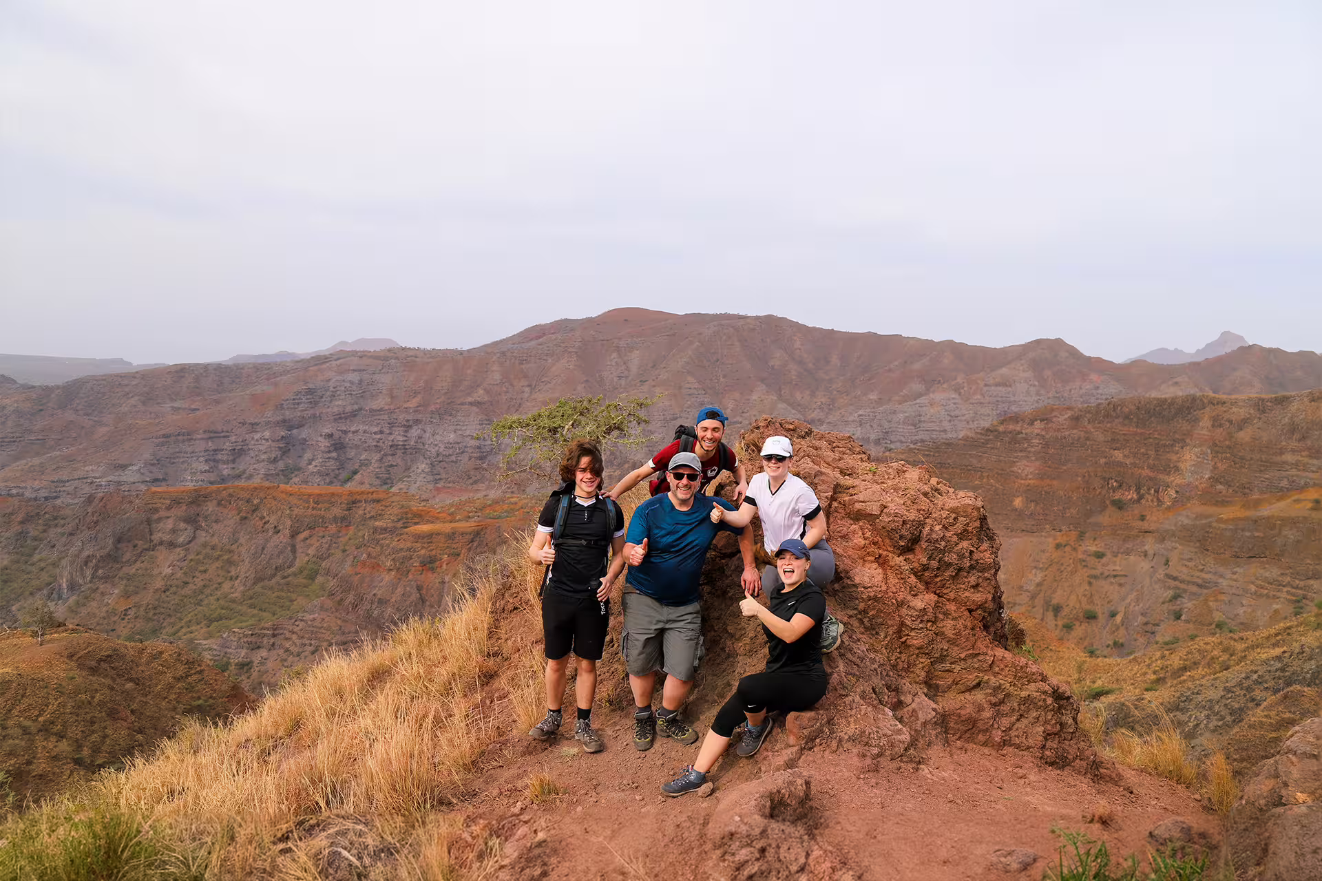 Group of hikers celebrating on a rocky crest in Monte Tchota Natural Park, with expansive mountain vistas in the background.