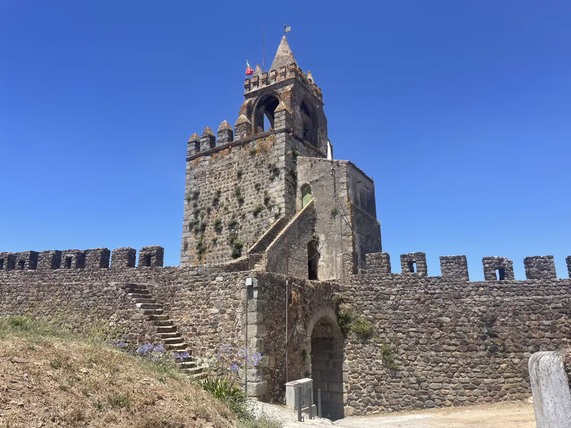 Historic Montemor-o-Novo Castle tower with stone walls and steps, set against a vibrant blue sky backdrop.