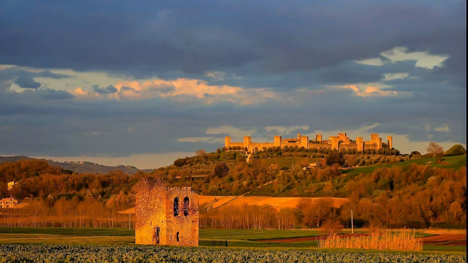 Monteriggioni's ancient fortified walls glowing in warm sunset light, surrounded by rolling Tuscan countryside.