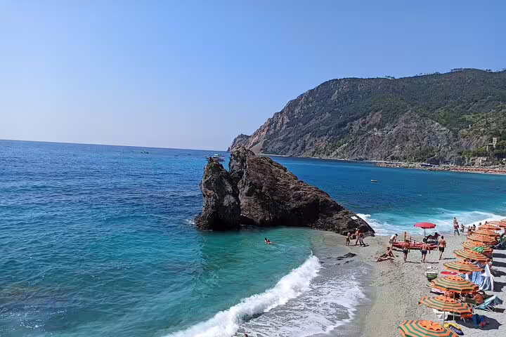 Colorful umbrellas and sunbathers on Monterosso al Mare beach in Cinque Terre, with turquoise Ligurian Sea and cliffs