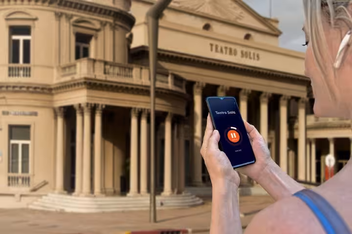 Tourist holding smartphone with audio guide app in front of Teatro Solis in Montevideo