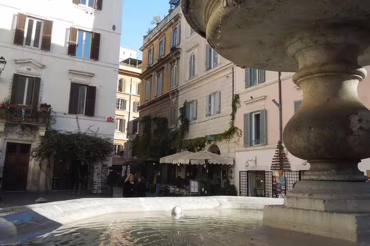 Historic Monti district piazza with charming fountain, ivy-covered buildings, and outdoor cafe on Rome sightseeing tour