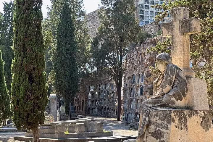 Sculpture and towering trees along tranquil Montjuïc Cemetery path, showcasing hidden art and serene views during the tour.