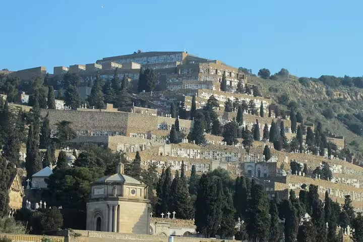 Terraced rows of Montjuïc Cemetery on a hillside, showcasing historical architecture and lush greenery under a clear blue sky.
