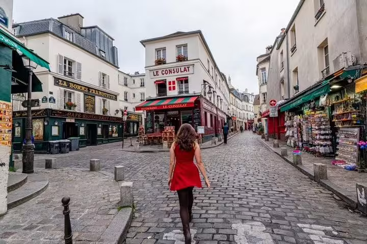 Woman in red dress walking cobblestone street toward Le Consulat café in Montmartre, Paris