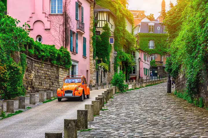 Vintage orange Citroën 2CV on a charming cobblestone street in Montmartre, Paris, surrounded by ivy-covered buildings