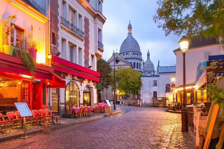 Cobblestone street in Montmartre with café terraces and Sacré-Cœur Basilica at dusk, Paris
