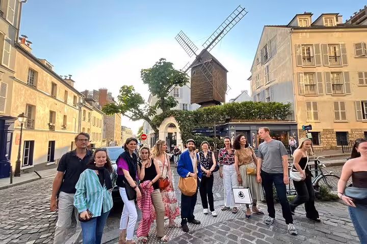 Tour group posing in front of historic Montmartre windmill on cobblestone street in Paris