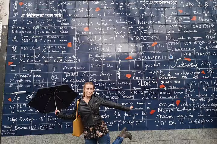 Woman with umbrella posing joyfully in front of the Je t'aime Wall in Montmartre, Paris