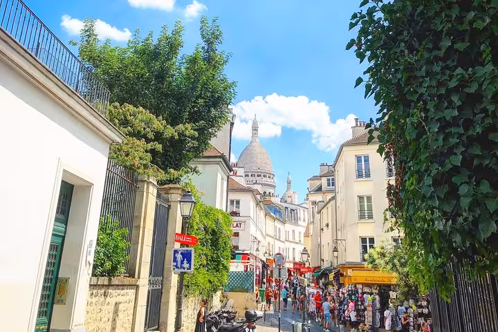 Cobblestone street in Montmartre with Sacré-Cœur basilica dome rising above Parisian buildings on a sunny day