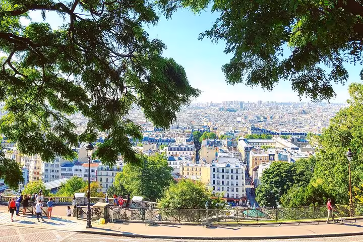 Panoramic view of Paris cityscape from Montmartre hill with lush trees and tourists on sunny morning