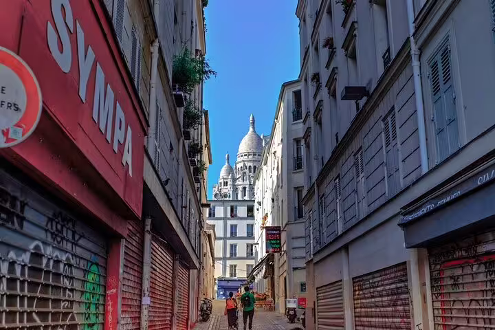 Narrow Montmartre street with Sacré-Cœur basilica dome visible between Parisian buildings