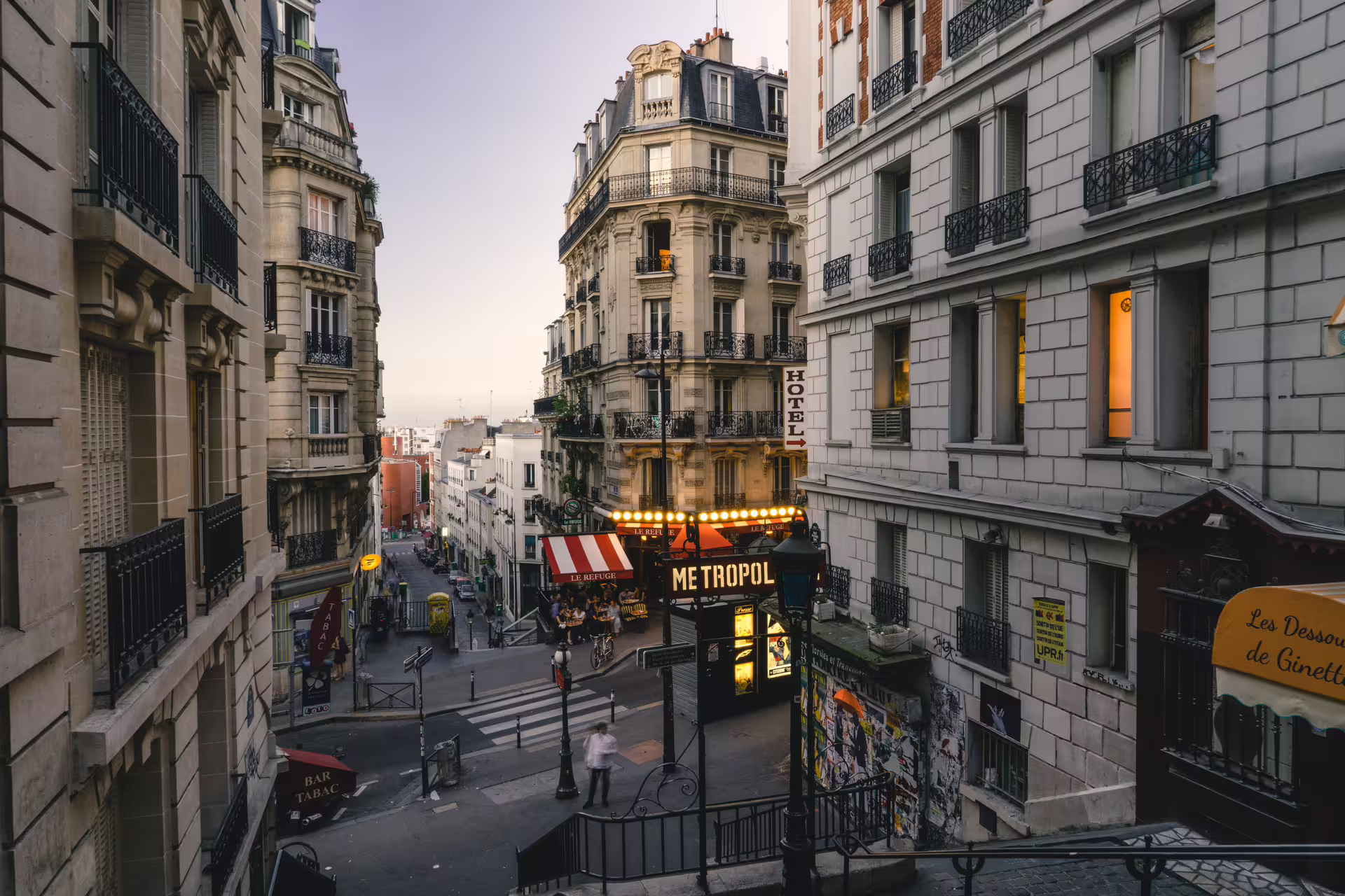 Charming Montmartre street corner at dusk with Le Refuge restaurant, Metropol sign, and Haussmann buildings in Paris
