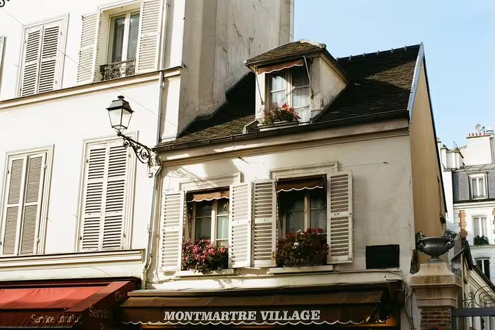 Montmartre Village sign on charming Parisian building with white shutters and flower boxes