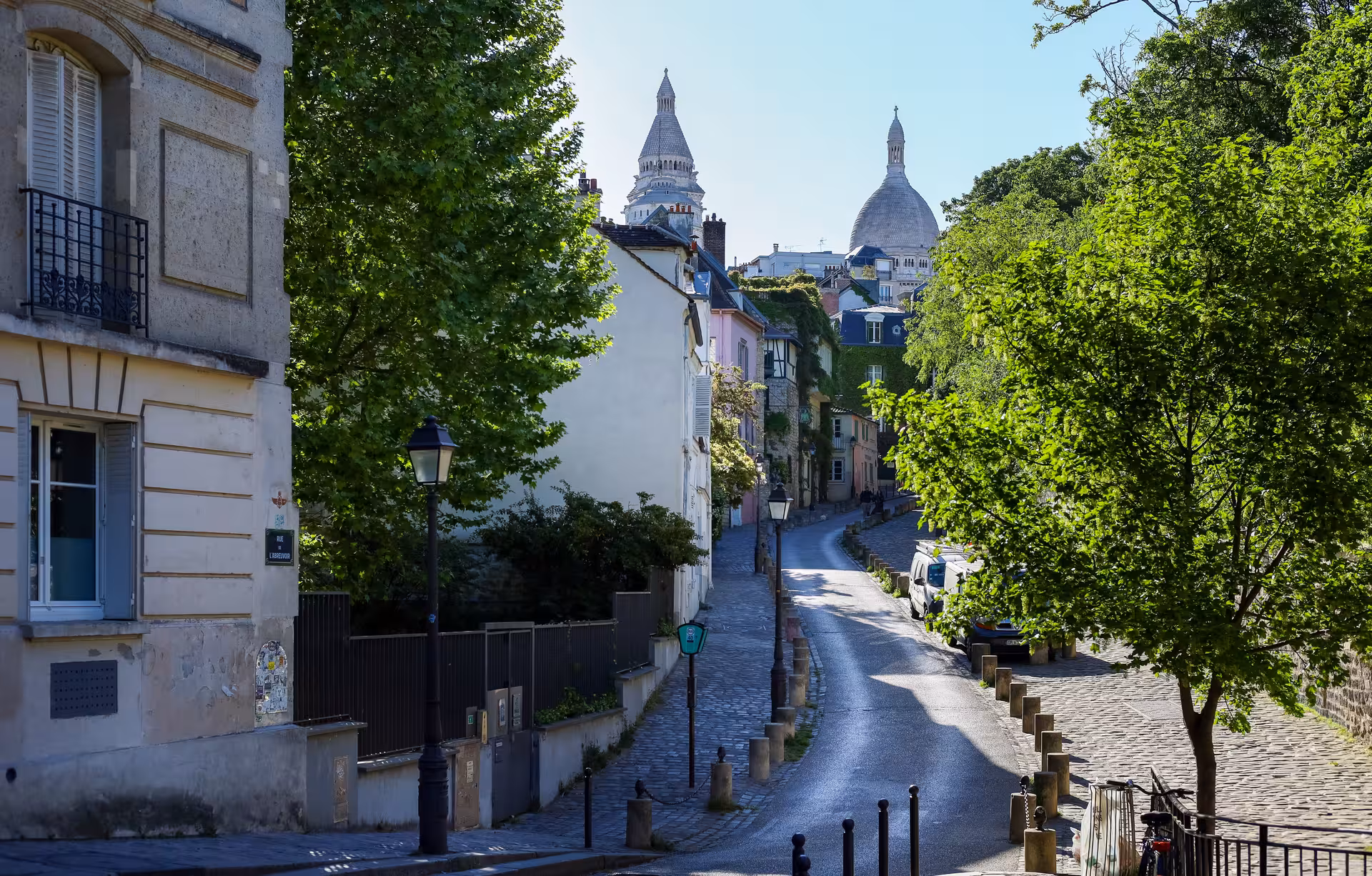 Cobblestone street in Montmartre with Sacré-Cœur Basilica domes visible above colorful Parisian buildings