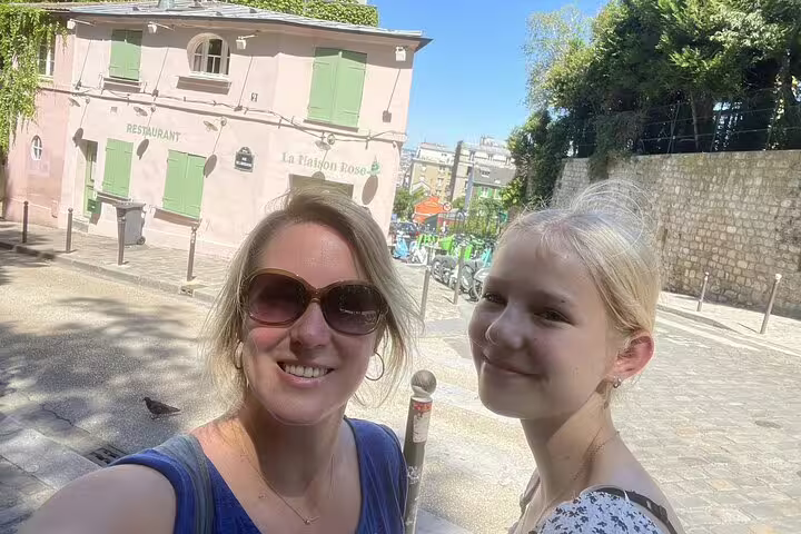 Two women smiling in front of La Maison Rose restaurant in Montmartre, Paris on a sunny day