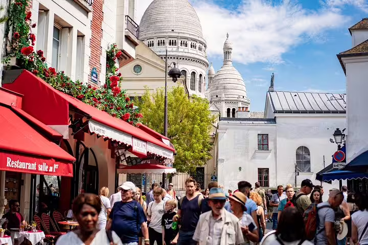 Crowded Montmartre street with Sacré-Cœur Basilica dome and red-awning café in Paris