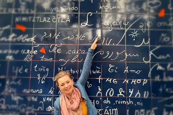 Smiling woman pointing at the Wall of Love with multilingual phrases in Montmartre, Paris
