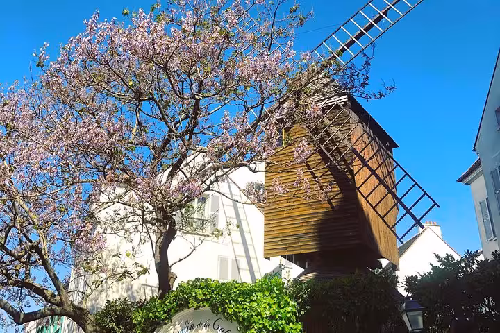 Moulin de la Galette windmill with pink blossoming tree in Montmartre Paris under blue sky