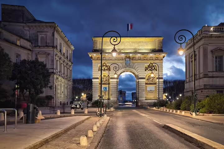 Illuminated Arc de Triomphe gate in Montpellier at night with French flag and ornate lampposts