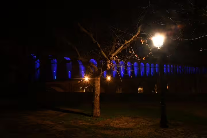 Historic Montpellier aqueduct lit in blue at night with bare trees and street lamp