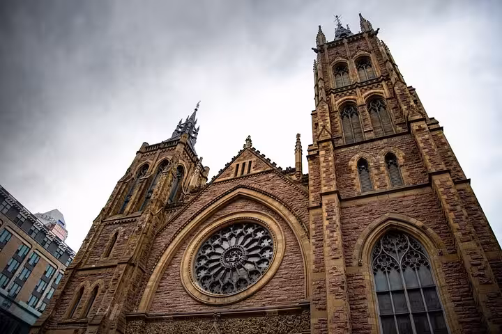 Gothic stone church with rose window and tall tower in Montreal under dramatic cloudy sky