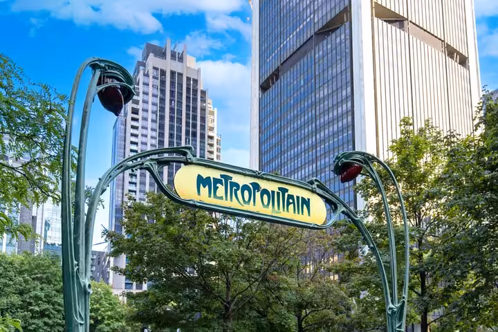 Art Nouveau Metropolitain subway sign in Montreal with green ironwork and yellow lettering, trees and skyscrapers behind
