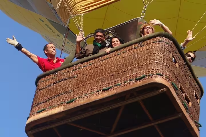 Smiling passengers waving from a hot air balloon basket during a scenic tour over Igualada and Montserrat.