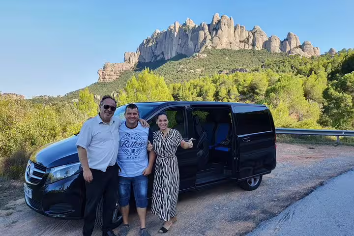Tourists posing with a van against the scenic backdrop of Montserrat's rugged mountain landscape.