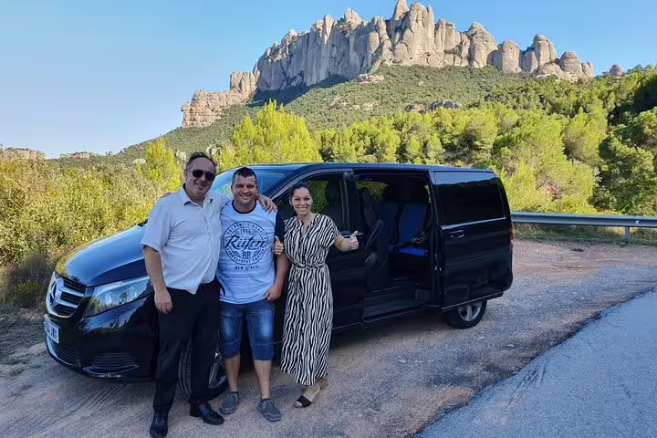 Travelers pose by a van with the stunning Montserrat mountains in the background on the Montserrat Tour.