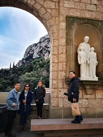 Group enjoying the Montserrat Private Tour with a scenic view, including a historic statue, lush landscape, and archway.