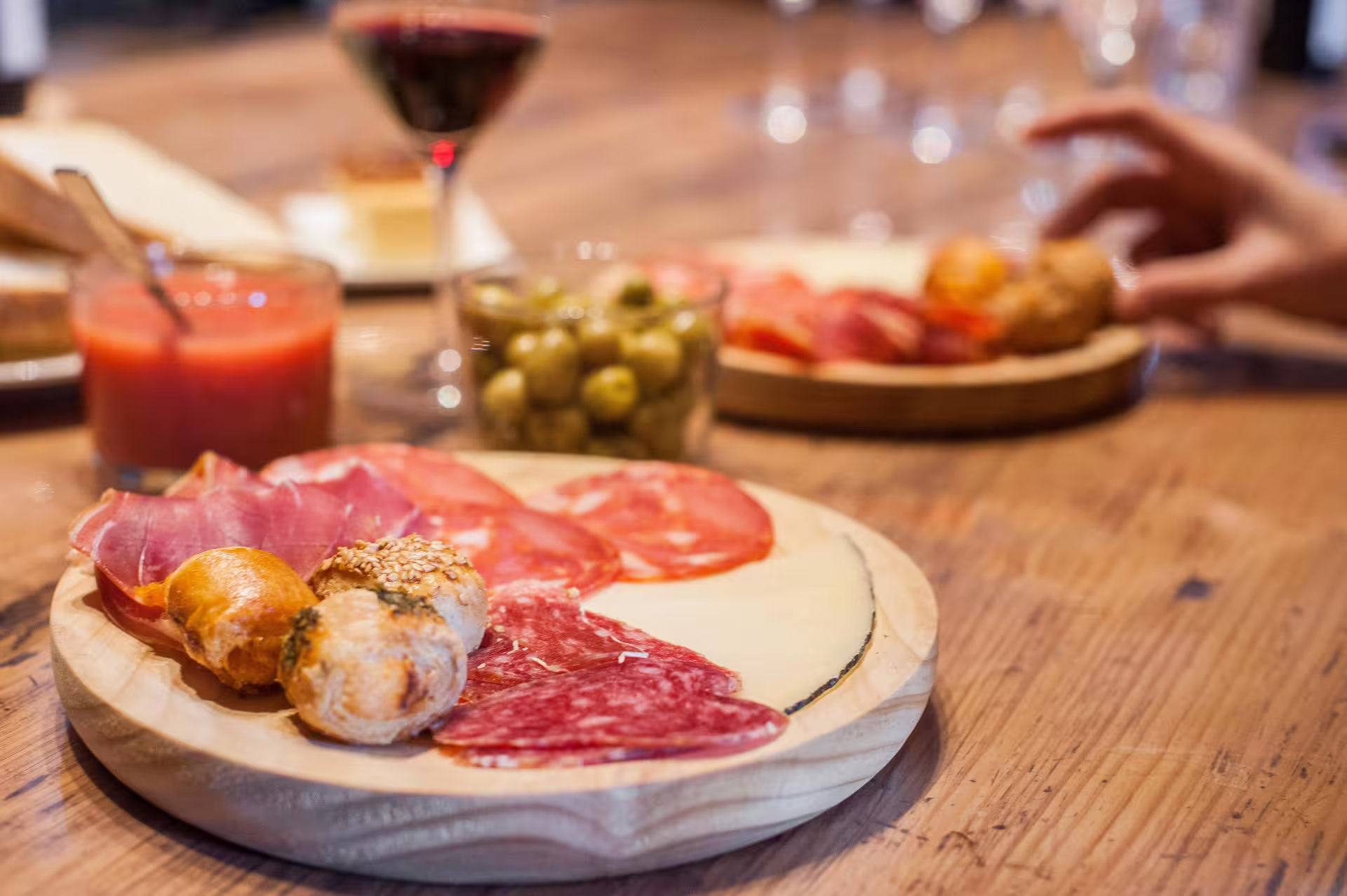 A rustic wooden table set with a variety of Spanish tapas, olives, cold cuts, and a glass of red wine, perfect for a Montserrat culinary tour.