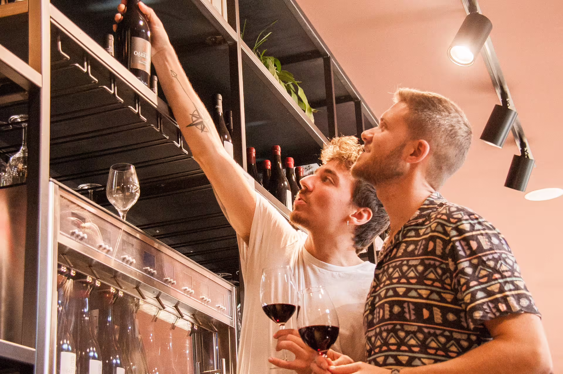 Two men selecting a wine bottle from a shelf during the Montserrat food and wine tour, showcasing wine exploration.