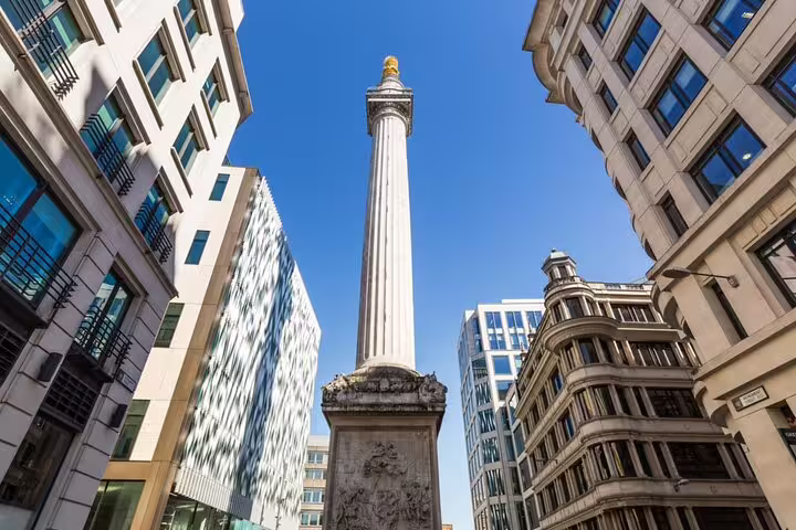 The Monument to the Great Fire of London standing tall among modern city buildings under a clear blue sky
