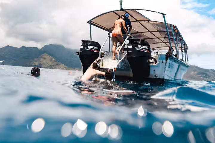 Snorkelers entering blue ocean water from a Suzuki-powered boat near Moorea mountains