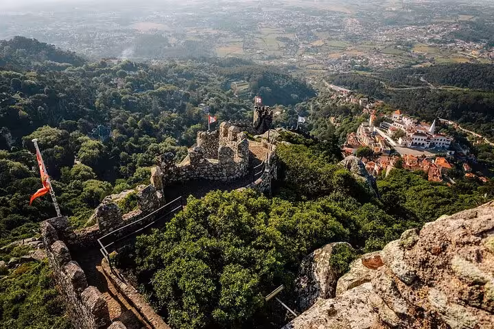 Breathtaking aerial view of the ancient Moorish Castle in Sintra surrounded by lush greenery and historic architecture.