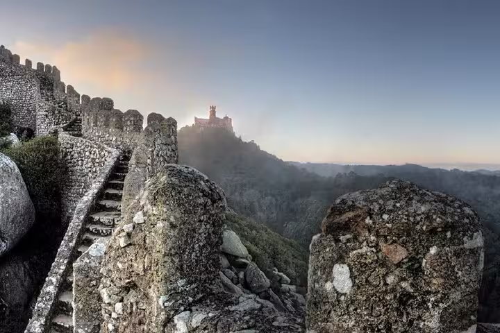 Ancient stone walls of the Moorish Castle in Sintra with a view of the Pena Palace at sunrise during a private half-day tour.