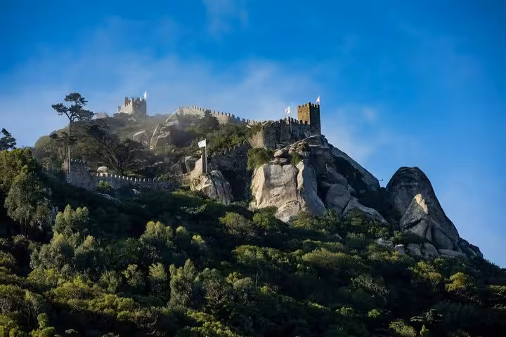 Majestic Moorish Castle ruins with stone walls and towers set against a backdrop of rugged hills and blue sky in Sintra.