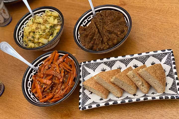 Assorted Moroccan appetizers including spiced potatoes, carrot salad, minced meat stew, and crispy bread on a wooden table.