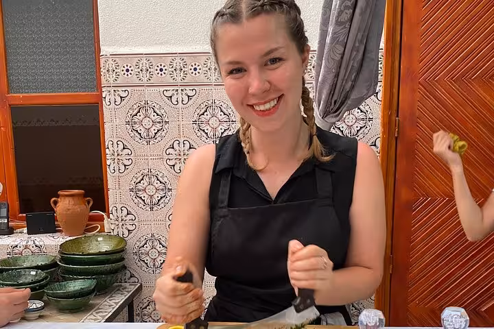 Woman smiling while chopping ingredients in a Moroccan cooking class with traditional kitchenware in the background.