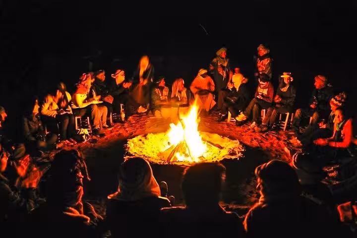 Tour group enjoying a vibrant nighttime campfire experience in the Moroccan desert on a Fes to Marrakech journey.