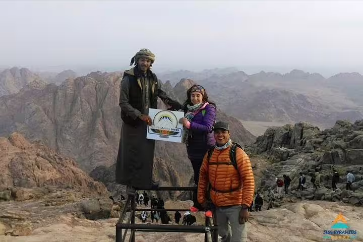 Hikers pose at Moses Mountain summit on a private Sinai tour from Taba, with rugged desert peaks behind