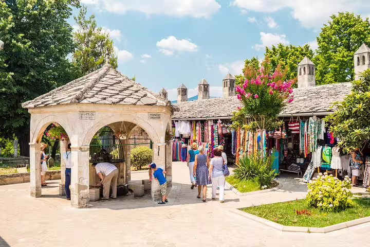 Mostar bazaar near Stari Most with souvenir stalls and historic stone well, stop on Makarska Riviera day tour
