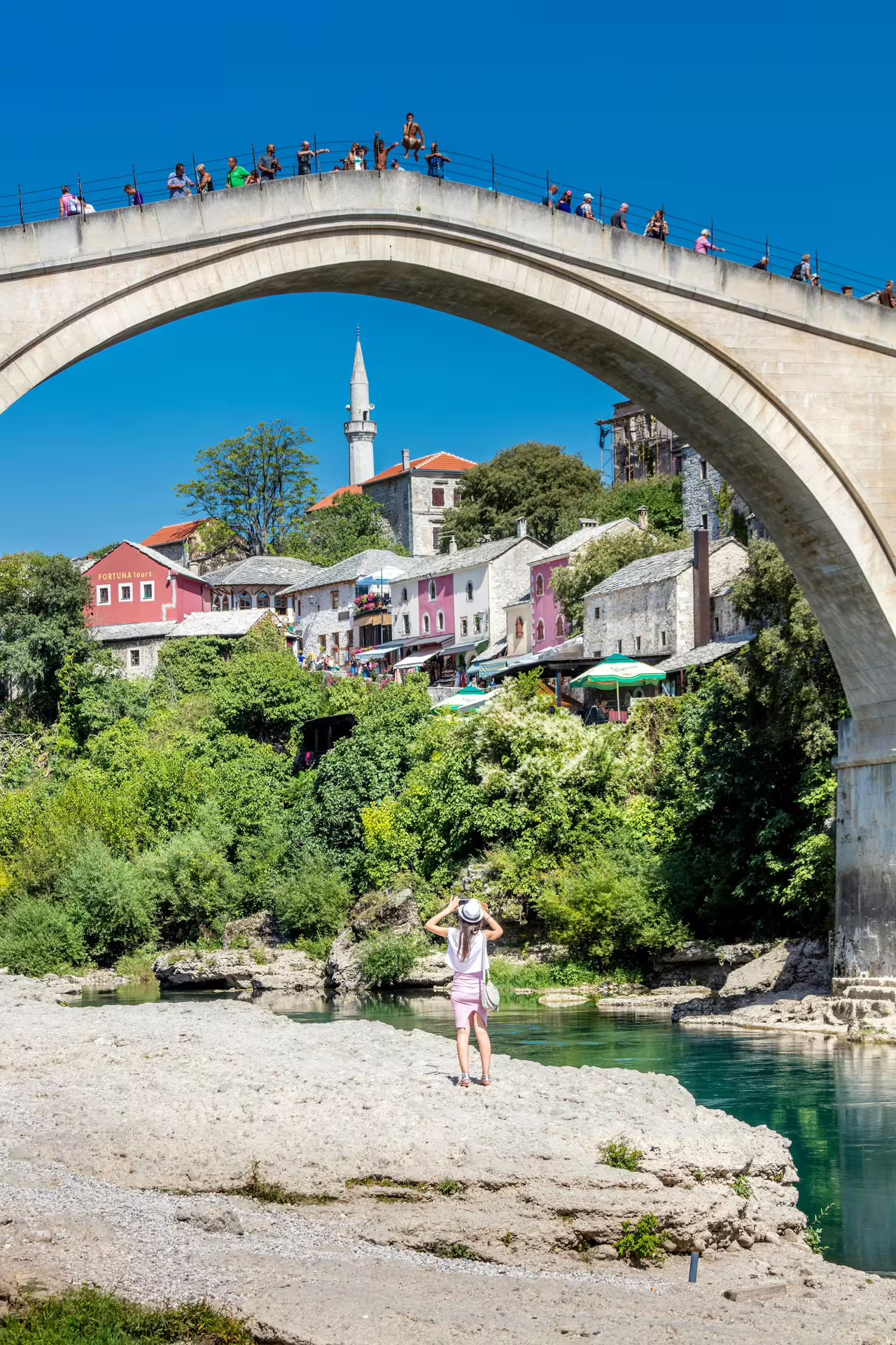 Tourist under Mostar Old Bridge with minaret views, highlight of the Mostar city tour from Dubrovnik
