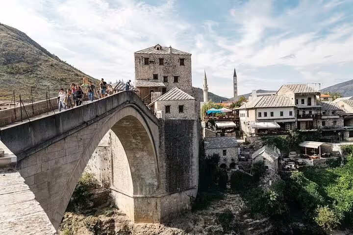 Tourists walking across Mostar Stari Most in Bosnia, cultural stop on scheduled Mostar & Kravice tour